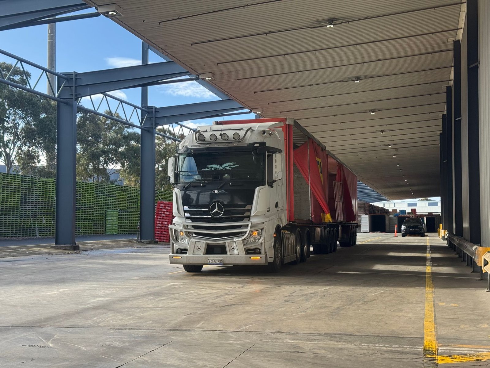Tractor unit with a flatbed trailer backed under a covered loading bay in morning light